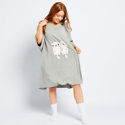 Woman wearing a gray oversized dress with cartoon otters on front, smiling and looking down